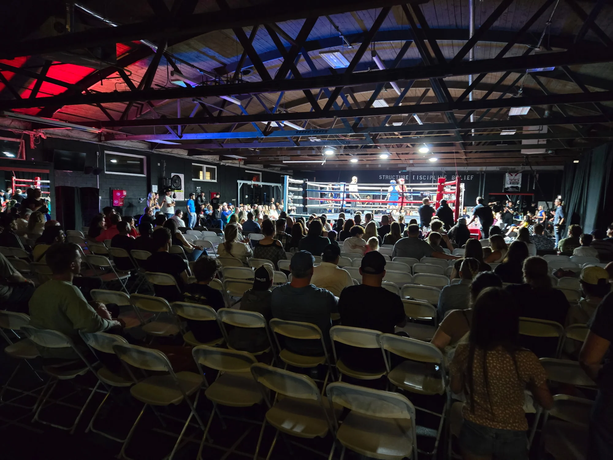 A lit boxing ring surrounded by spectators at a local fight night